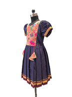 A traditional Mexican-style dress displayed on a black dress form mannequin against a white background. The dress features a dark navy blue polka-dot skirt with gold and burgundy trim, a pink floral embroidered bodice, and matching navy puff sleeves with gold trim. - House of Kritee