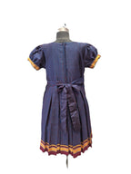 A short-sleeve dress displayed on a mannequin from the back, featuring a blue and red patterned fabric with yellow and burgundy striped cuffs and hem. - House of Kritee