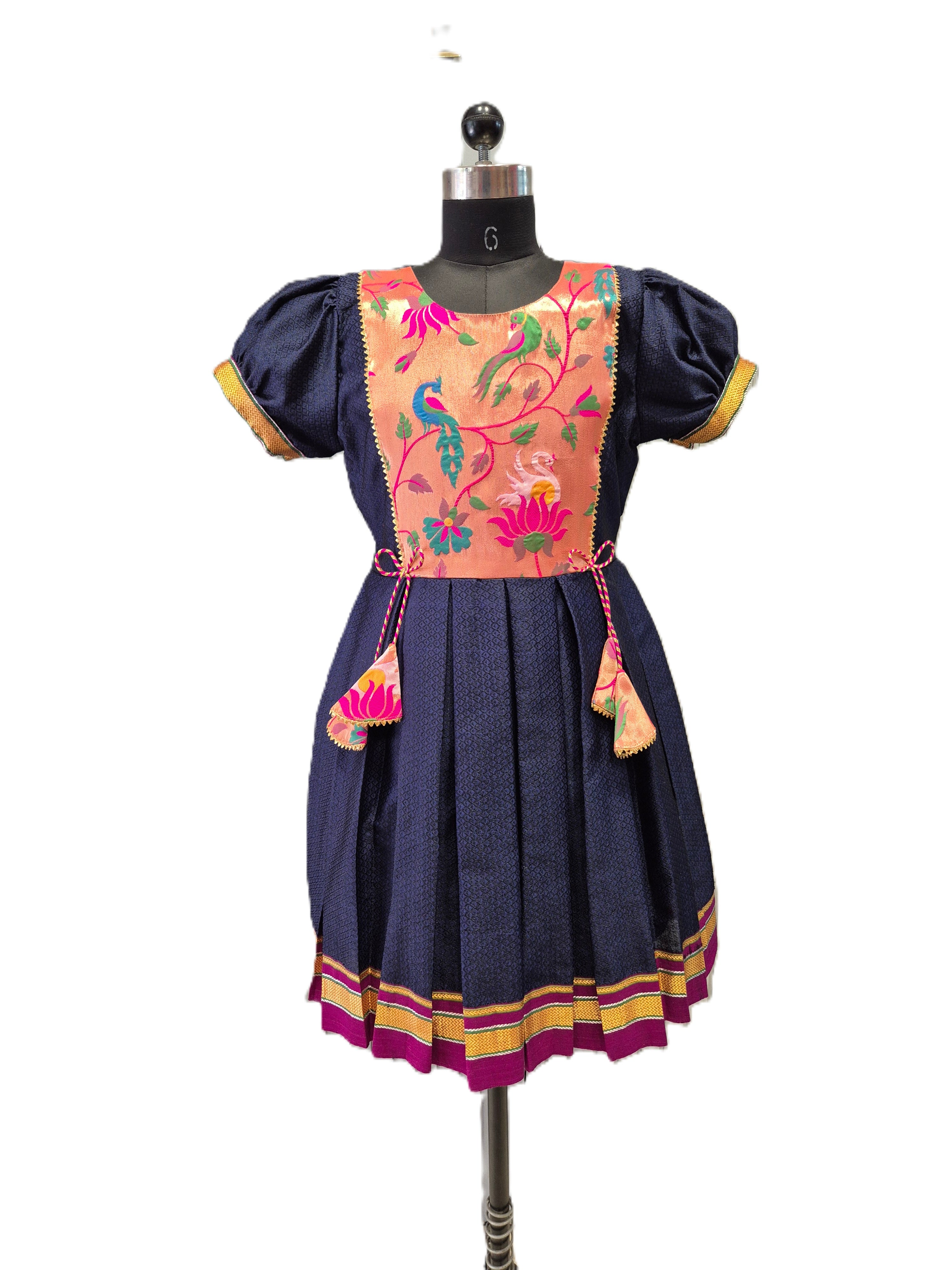 A traditional Mexican-style dress displayed on a mannequin, featuring a navy blue skirt and bodice with a peach-colored embroidered yoke panel depicting floral and bird motifs. - House of Kritee