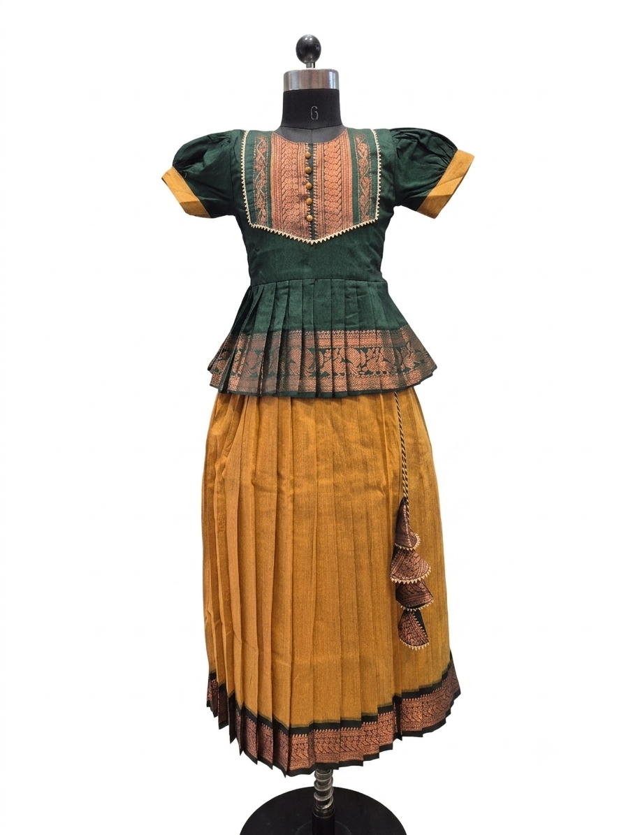 A traditional short-sleeved dress displayed on a black mannequin against a white background. The dress features a dark green bodice with gold and brown embroidered details, a matching green peplum waist, and a pleated mustard yellow skirt with a brown patterned border and tassel accents - House of Kritee