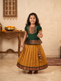 Happy young girl wearing a premium green and mustard-gold traditional Kalyani Gadhawal Parkar-Polka dress set inside a warm cream room - House of Kritee