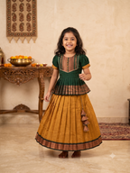 Happy young girl wearing a premium green and mustard-gold traditional Kalyani Gadhawal Parkar-Polka dress set inside a warm cream room - House of Kritee