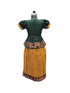 A vintage folkloric costume dress displayed on a mannequin from the back, featuring a dark green short-sleeved top with mustard yellow cuffs, a patterned waistband, and a matching pleated mustard yellow skirt - House of Kritee