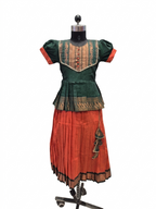 A traditional Indian outfit displayed on a black dress form mannequin, featuring a dark green embroidered blouse with orange sleeves and a matching pleated orange skirt with gold borders - House of Kritee