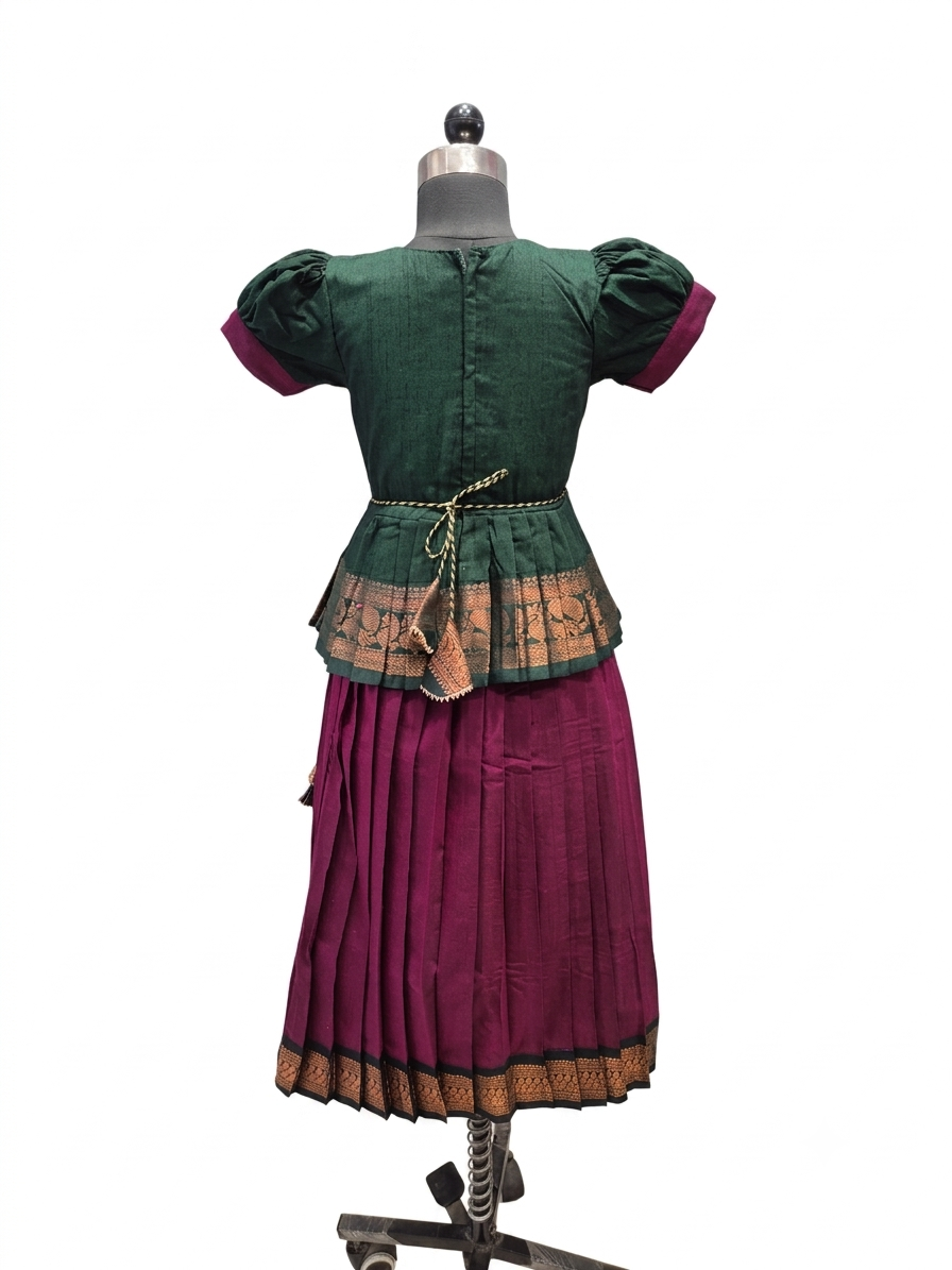 A traditional two-piece outfit displayed on a dress form, featuring a dark green short-sleeve top with purple cuffs and a gold patterned peplum waist detail, paired with a pleated magenta skirt with a gold border. - House of Kritee