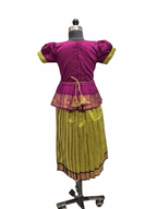 A traditional Indian outfit displayed on a dress form mannequin, featuring a magenta purple short-sleeve top with yellow-green cuffs and a gold-trimmed peplum waist, paired with a pleated olive green skirt with a gold border. - House of Kritee