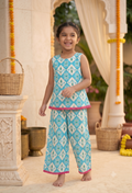 Happy young Desi digital girl smiles and poses in a turquoise blue and white Ikat print sleeveless peplum trousers co-ord set with pink bobble trim in a premium garden patio setting