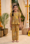 A young Desi digital girl smiles and happily poses in a mustard pure cotton two-piece peplum and trouser set featuring a traditional floral print