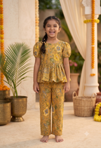 A young Desi digital girl smiles and happily poses in a mustard pure cotton two-piece peplum and trouser set featuring a traditional floral print