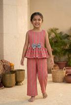 Happy Desi digital girl smiling in a premium coral peach cotton peplum co-ord set with a grey waist bow and matching trousers in a soft cream garden background