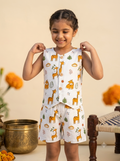 Happy Desi digital girl smiling and wearing a premium white cotton co-ord set featuring a giraffe print sleeveless waistcoat with wooden buttons and matching shorts in a blurred garden background setting