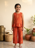 Happy Desi digital girl smiling in a premium rust orange cotton co-ord set featuring yellow traditional puppet print peplum top and trousers in a soft cream garden background