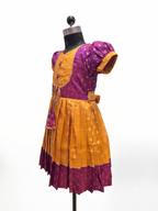 A traditional Indian salwar suit set displayed on a black dress form mannequin. The set features a mustard yellow pleated skirt with a magenta purple border and a matching mustard yellow waist tie, paired with a magenta purple short-sleeve blouse decorated with gold polka dots and a gold embroidered border. - House of Kritee