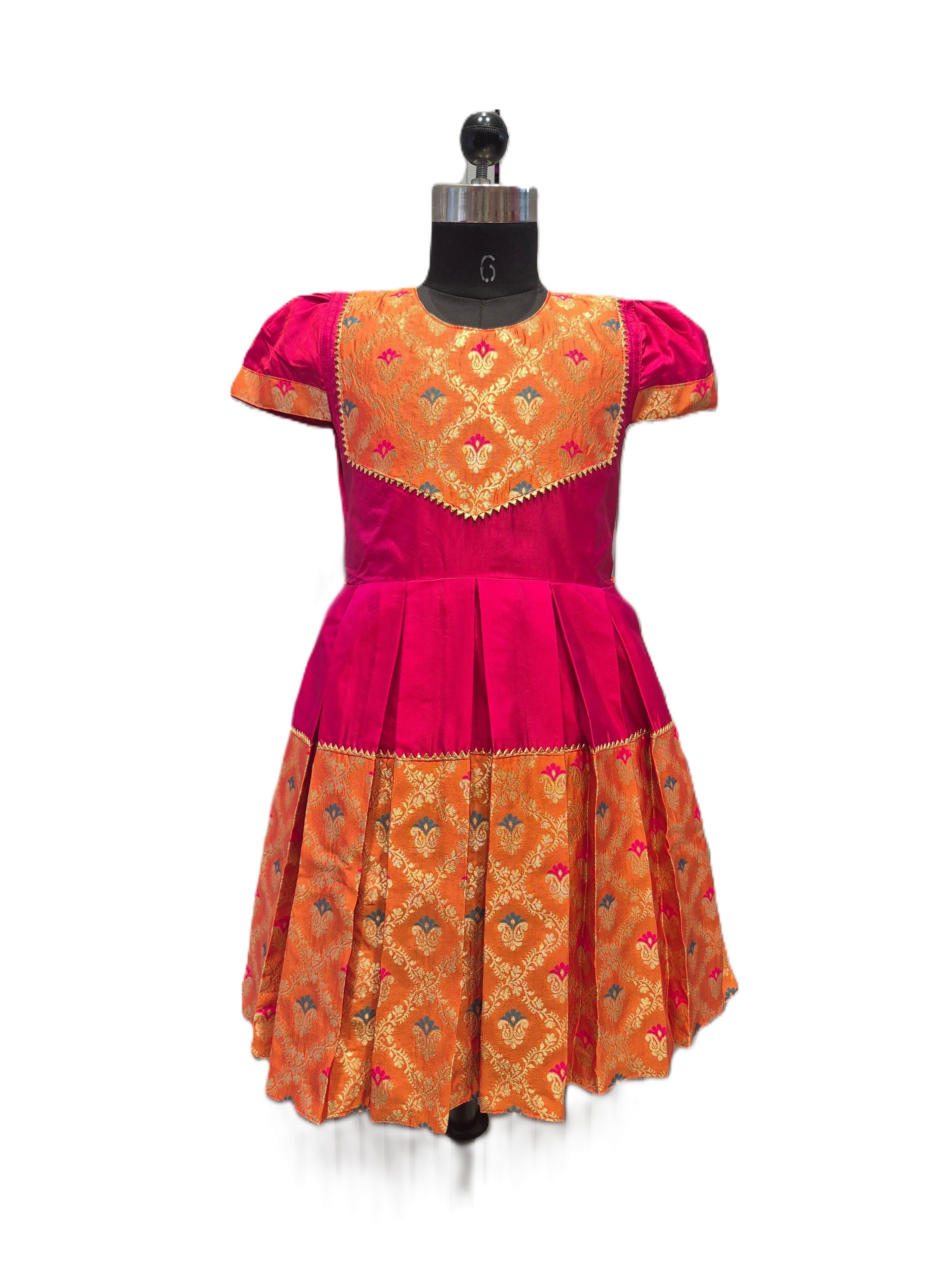 A traditional Indian salwar suit dress displayed on a black dress form mannequin. The dress features a bright magenta pink body with a heavily embroidered orange and gold brocade yoke, short puff sleeves, and a matching pleated skirt with an orange and gold patterned border. - House of Kritee