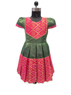 A green and pink traditional dress displayed on a black dress form mannequin against a plain white background. The dress features a green body with a bright pink embroidered yoke and a matching pink patterned hem. - House of Kritee