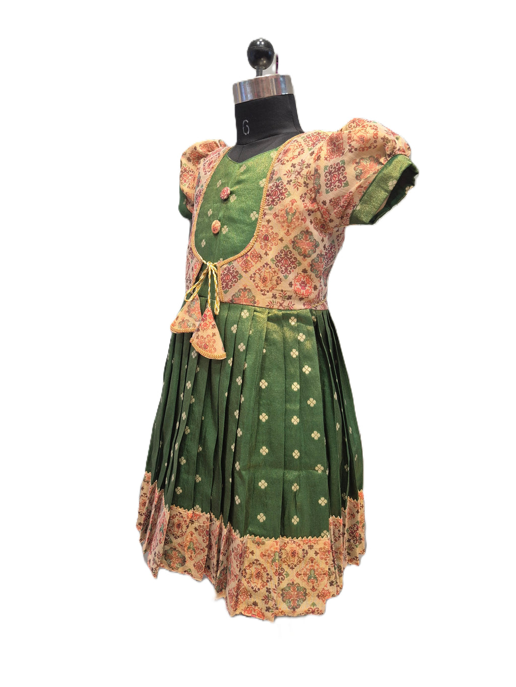 A traditional Indian dress displayed on a black dress form mannequin against a plain white background. The dress features a dark green skirt with small gold motifs and a matching green border, paired with a beige and green heavily patterned blouse. - House of Kritee