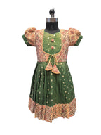 A green medieval-style dress displayed on a black dress form mannequin against a white background. The dress features a green bodice with a patterned beige and pink overlay, puffed sleeves, a tie at the waist, and a patterned skirt. - House of Kritee