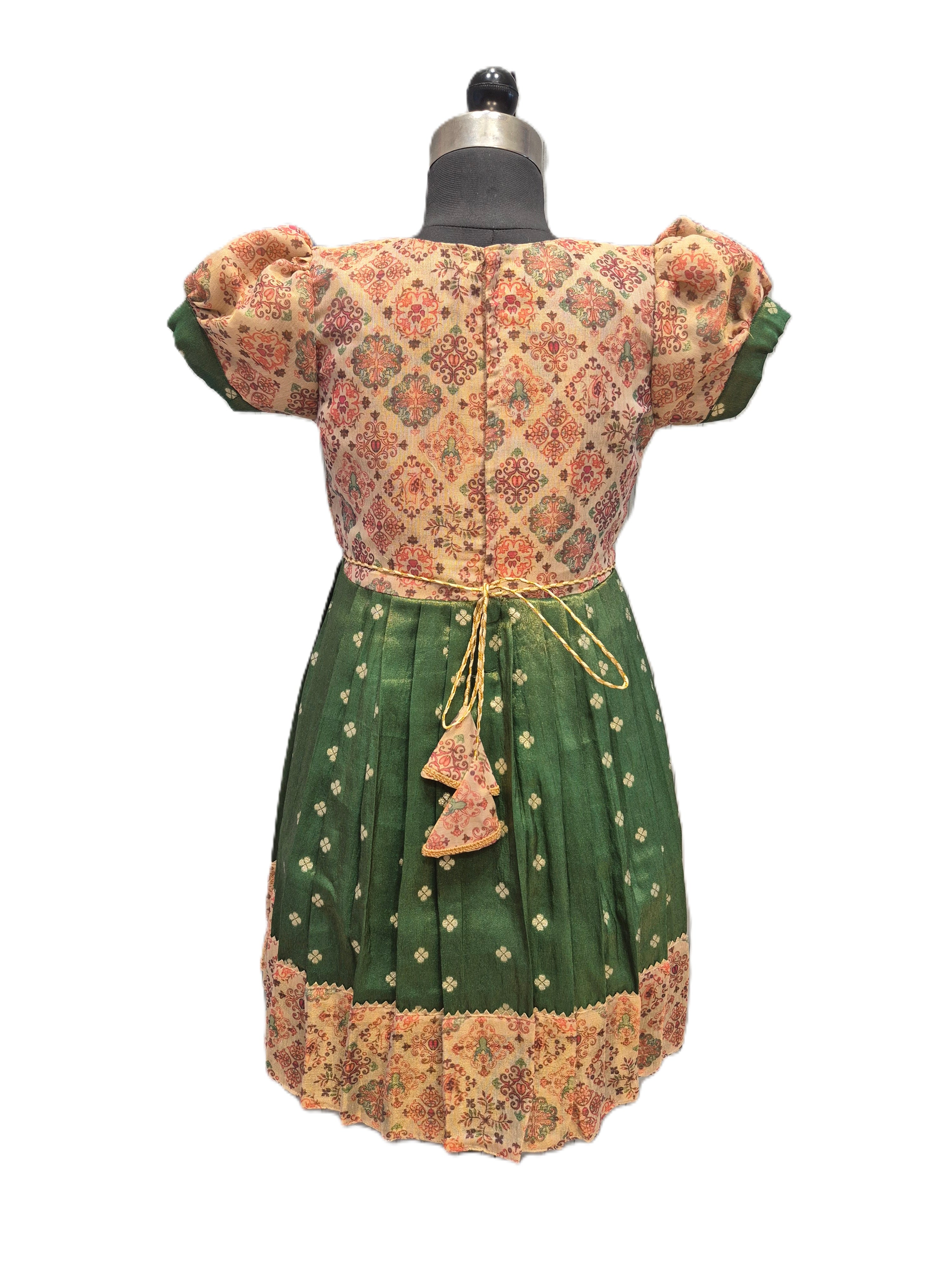 A traditional Mexican dress displayed on a dress form, featuring a green skirt with gold floral embroidery and lace trim, and a patterned beige and orange bodice with puff sleeves. - House of Kritee