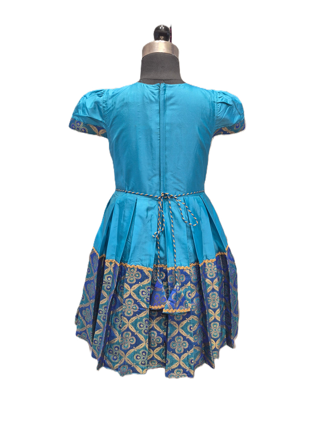 A blue short-sleeve dress shown from the back on a dress form mannequin, featuring a pleated skirt with a blue, gold, and green patterned border. - House of Kritee