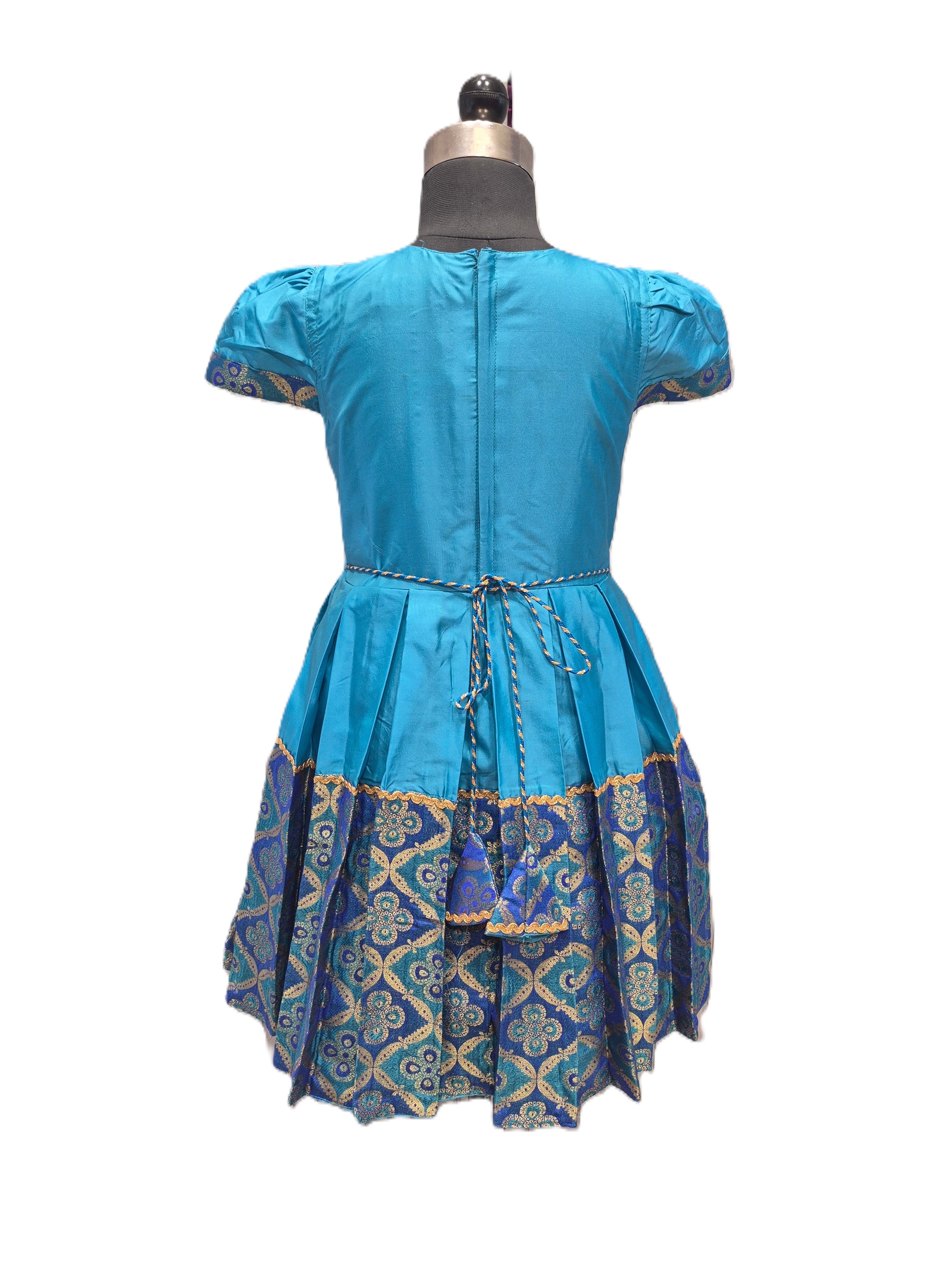 A blue short-sleeve dress shown from the back on a dress form mannequin, featuring a pleated skirt with a blue, gold, and green patterned border. - House of Kritee
