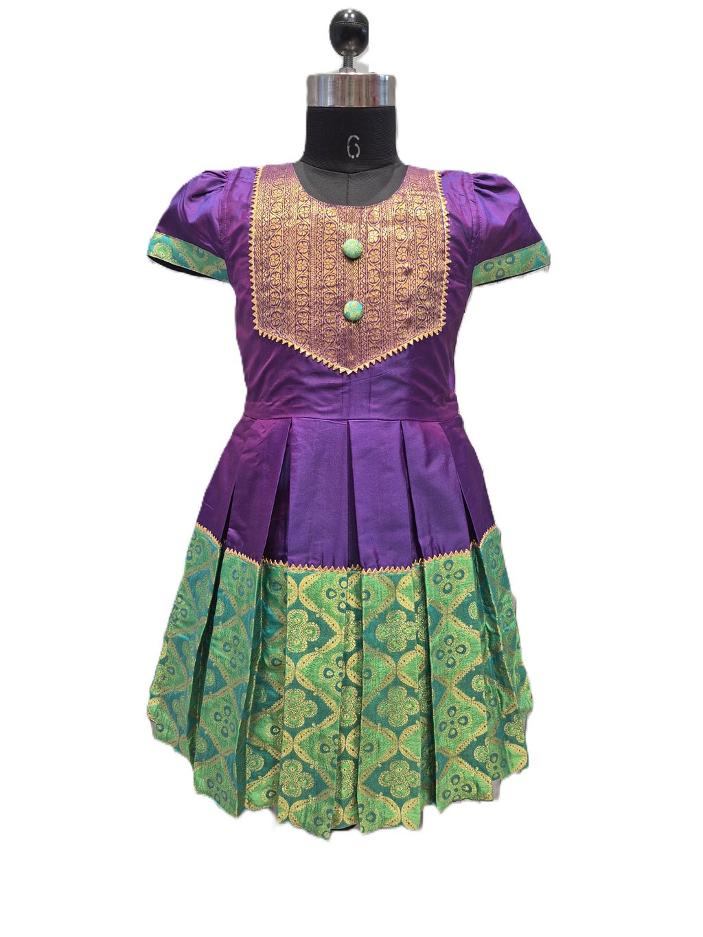 A purple and green traditional dress displayed on a black dress form mannequin against a plain white background. The dress features a purple bodice with a gold embroidered yoke and green patterned skirt panels. - House of Kritee