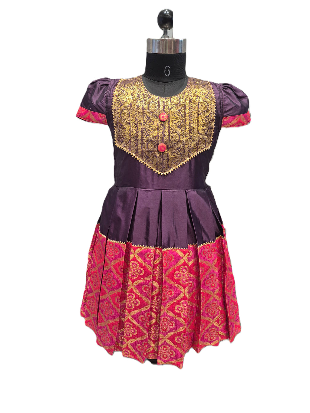 A traditional Indian girl's dress displayed on a black dress form mannequin. The dress features a deep purple bodice with a wide, ornate gold embroidered yoke, short puff sleeves with purple cuffs, and a pleated skirt with a bright pink and gold patterned brocade. - House of Kritee