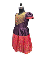 A purple and red traditional dress displayed on a black dress form mannequin against a white background. The dress features a purple bodice with gold embroidery, puffed short sleeves, and a red patterned skirt. - House of Kritee