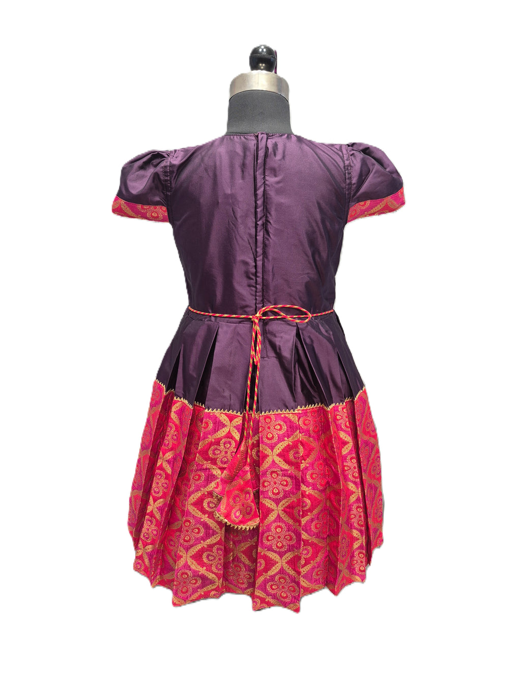 A purple and pink traditional dress displayed on a mannequin from the back, featuring a purple satin-like bodice with puff sleeves, a matching waist tie, and a pink patterned skirt. - House of Kritee