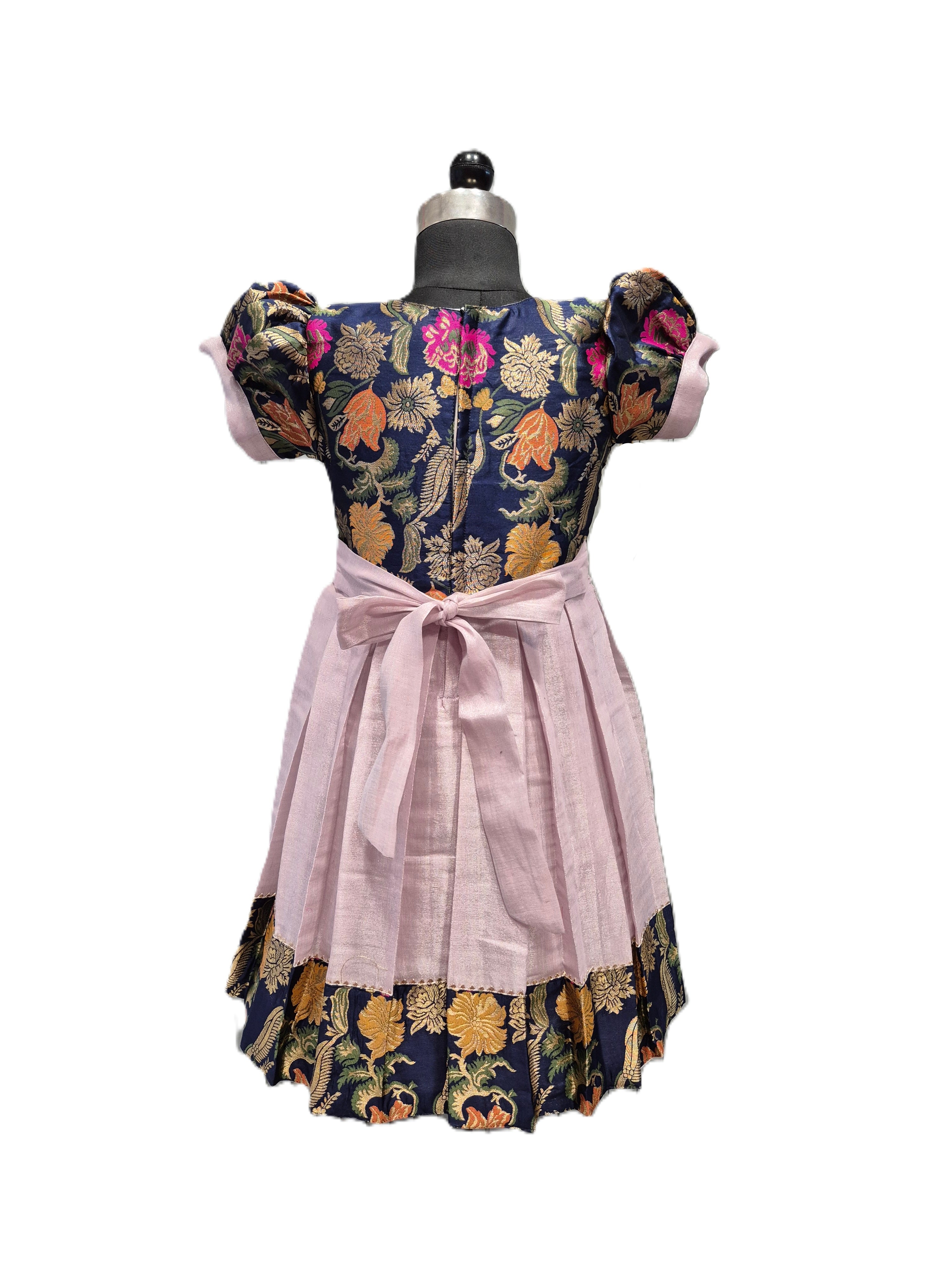 A vintage-style dress displayed on a black dress form mannequin against a white background. The dress features a navy blue floral bodice with pink, orange, and gold patterns, a light pink pleated skirt, and a matching pink waist bow. - House of Kritee