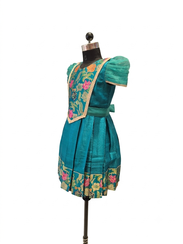 Happy Desi girl model wearing a teal blue silk knee length frock with floral jacquard bodice - House of Kritee