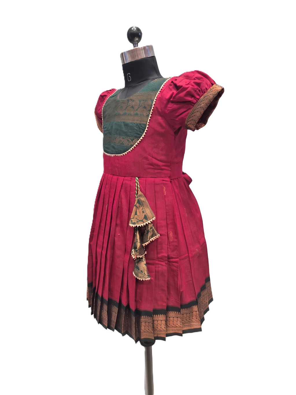 A traditional Indian salwar suit displayed on a dress form mannequin, featuring a deep magenta pink pleated skirt with a black and gold border, a dark green embroidered yoke, and matching pink puff sleeves. - House of Kritee
