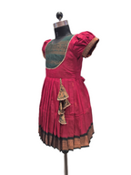 A traditional Indian salwar suit displayed on a dress form mannequin, featuring a deep magenta pink pleated skirt with a black and gold border, a dark green embroidered yoke, and matching pink puff sleeves. - House of Kritee