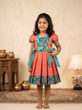 Happy young girl enjoying her premium coral and teal brocade silk knee-length ethnic frock dress inside a warm cream room- House of Kritee