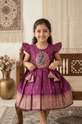 Young Desi girl wearing a happy purple silk ethnic frock with gold zari border and peacock motif