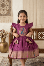 Young Desi girl wearing a happy purple silk ethnic frock with gold zari border and peacock motif