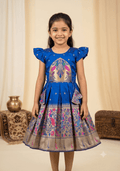 A happy young girl modeling a premium royal blue silk ethnic frock with a patterned skirt and decorative side pouches in a high-end cream background