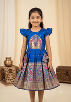 A happy young girl modeling a premium royal blue silk ethnic frock with a patterned skirt and decorative side pouches in a high-end cream background