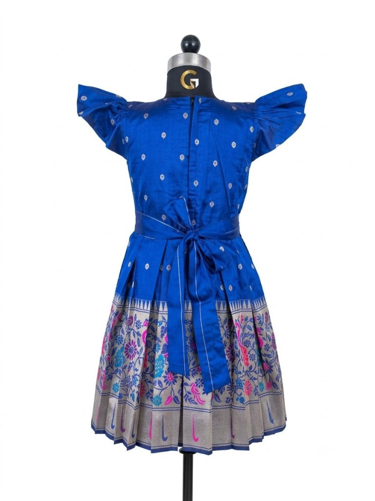 A happy young girl modeling a premium royal blue silk ethnic frock with a patterned skirt and decorative side pouches in a high-end cream background