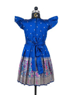A happy young girl modeling a premium royal blue silk ethnic frock with a patterned skirt and decorative side pouches in a high-end cream background