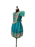 Happy Desi girl model wearing a teal blue silk knee length frock with floral jacquard bodice - House of Kritee