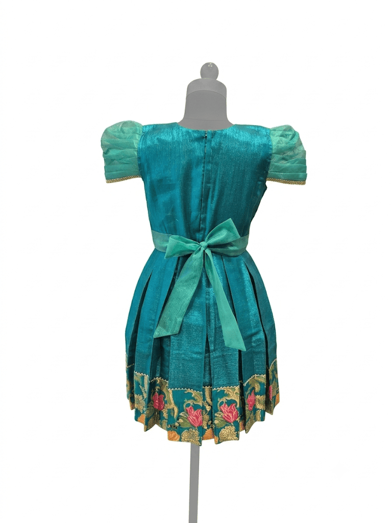 Happy Desi girl model wearing a teal blue silk knee length frock with floral jacquard bodice - House of Kritee