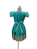 Happy Desi girl model wearing a teal blue silk knee length frock with floral jacquard bodice - House of Kritee