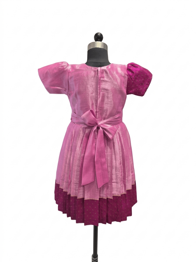"Happy young Indian girl model smiling in a premium dual-shade pink and magenta silk ethnic knee-length frock with gold borders and tassels"