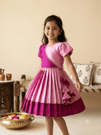 "Happy young Indian girl model smiling in a premium dual-shade pink and magenta silk ethnic knee-length frock with gold borders and tassels"