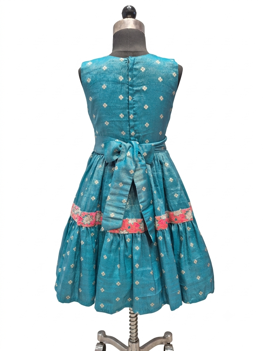 A sleeveless teal blue dress with small white floral prints and a pink patterned band near the waist, displayed on a dress form against a white background.