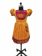 A traditional Indian salwar suit set displayed on a black mannequin. The set includes a mustard yellow salwar with a deep red and gold embroidered yoke, matching mustard yellow flutter sleeves, and a pleated skirt with a red and gold border.