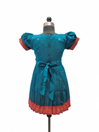 A teal blue cotton dress displayed on a mannequin, featuring puff sleeves with red cuffs, a matching waist tie, and a red patterned hem.