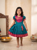 Happy young girl wearing a premium teal blue and magenta silk knee-length frock inside a beautifully decorated warm cream home - House of Kritee