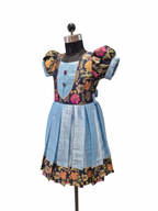 A children's dress displayed on a black mannequin against a plain white background. The dress has a light blue pleated skirt, a dark navy bodice with colorful floral embroidery, and puffed sleeves.  - House of Kritee