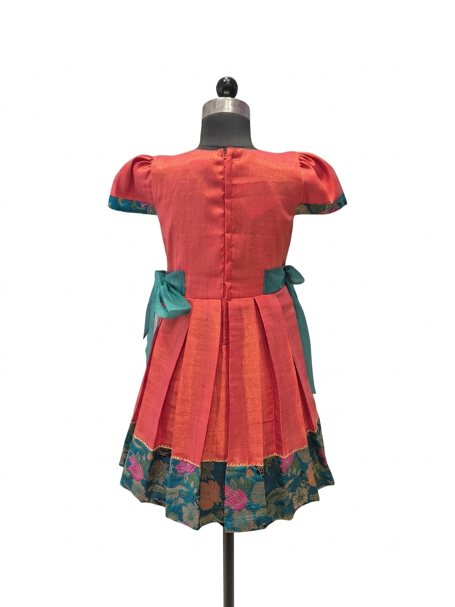 A short-sleeved dress displayed on a mannequin from the back, featuring a coral-red body, teal bow details at the waist, and a floral patterned border along the hem - House of Kritee